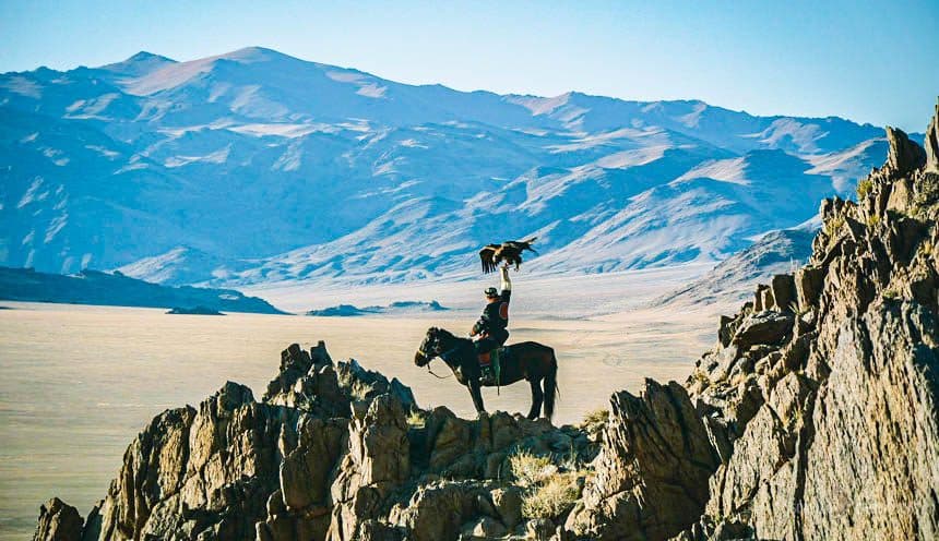 Eagle hunter raising his eagle on a mountain crag